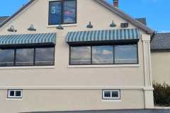 Custom-designed striped awnings with gooseneck lighting installed on a commercial building, providing both style and functionality.